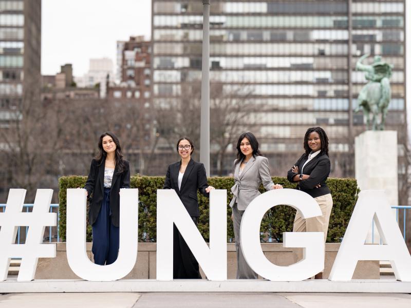 Four students stand behind large letters "#UNGA" dressed in business attire.