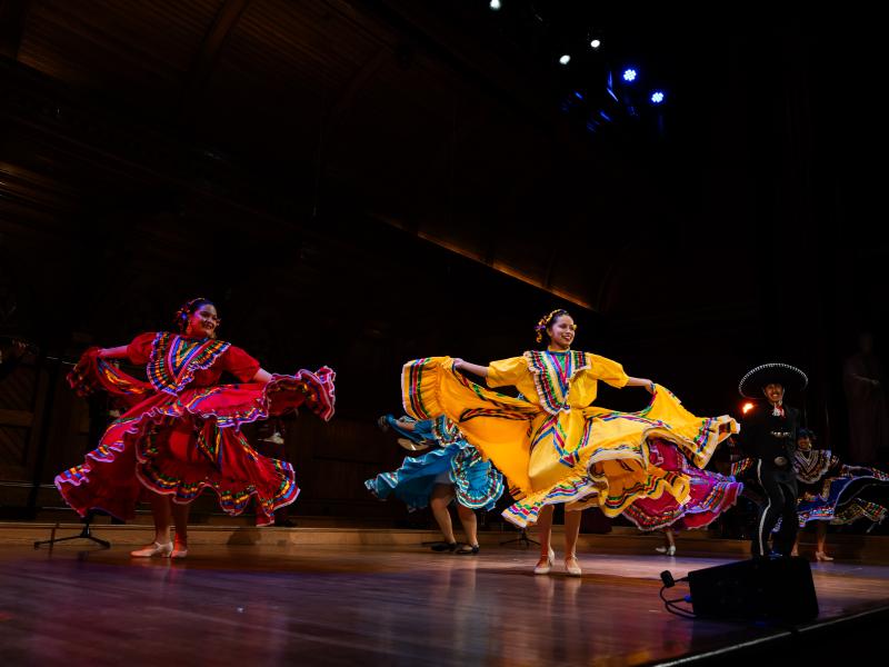 The Harvard Undergraduate Candela Latin Dance Troupe performing onstage during Cultural Rhythms in brightly colored dresses.