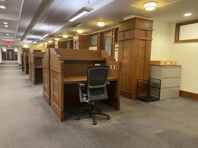 A singular black desk chair at a wooden cubicle.