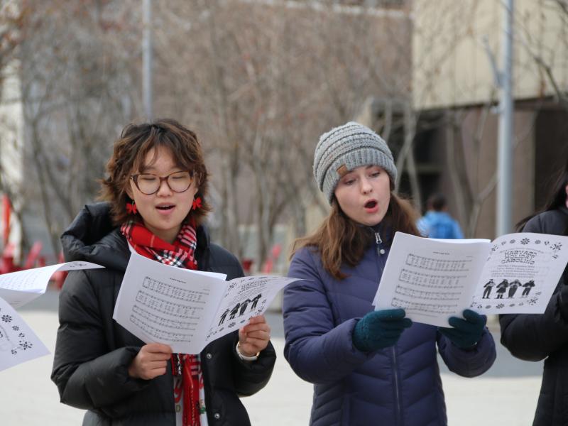 Two female students read sheet music while singing outside on the Harvard campus.