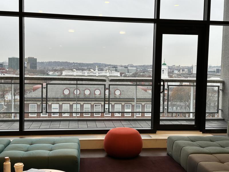 A red bean bag chair and green ottomans looking out a large window with an aerial view of Harvard.