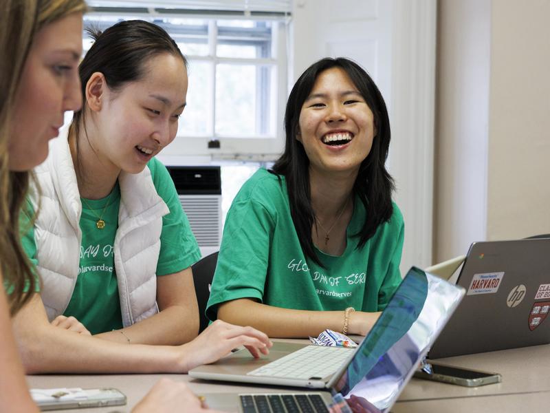 A female student smiling widely while looking at other volunteers seated beside her.