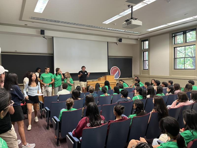 A classroom full of students wearing green shirts and listening to the speaker in the front of the room.