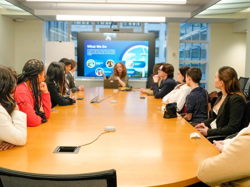 Students sitting around a table listening to a session.