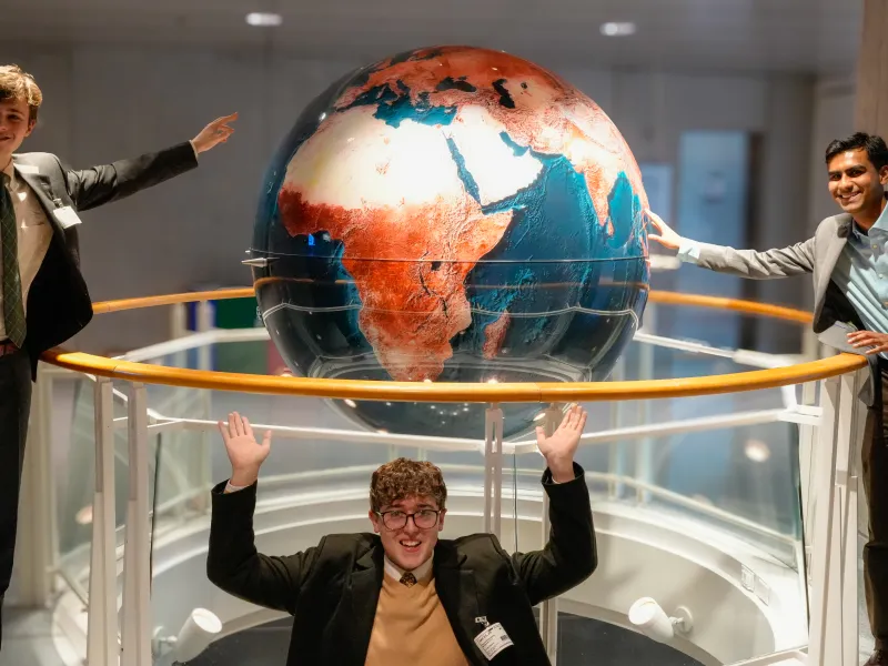 Three male students standing with a globe inside the World Bank Headquarters.
