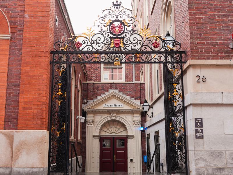  Ornate black and gold wrought-iron gate frames the red double-door entrance to Adams House.