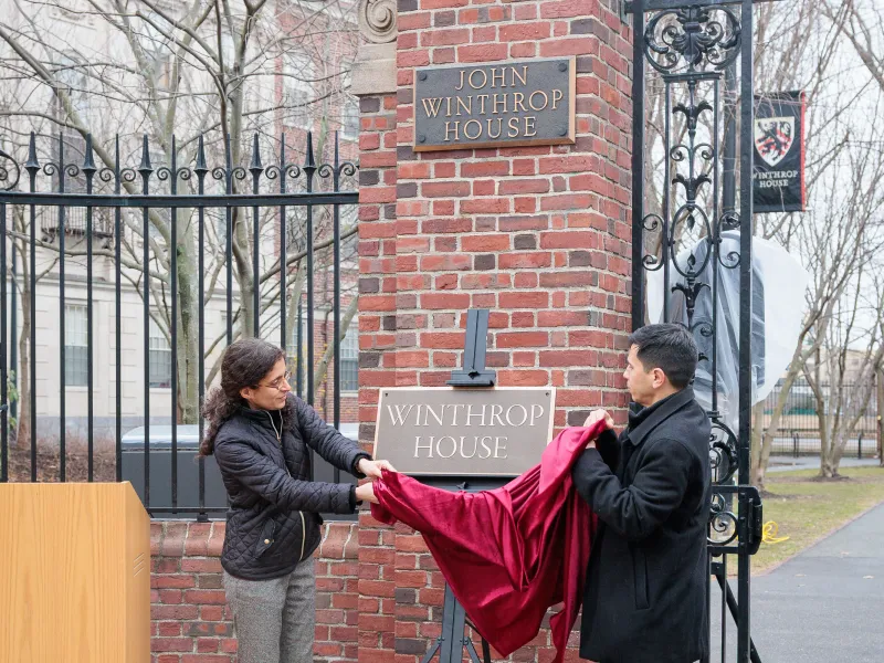 Two people unveil a new “Winthrop House” sign beneath the existing John Winthrop House gate plaque.