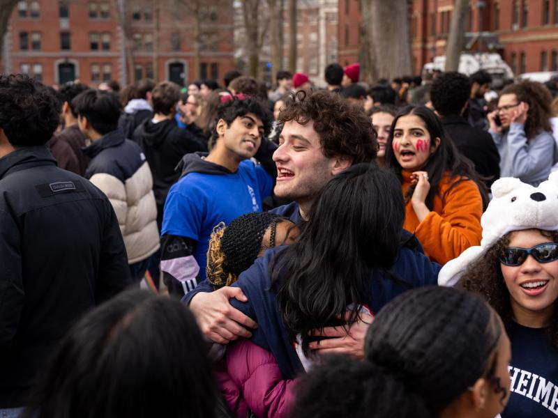 Students gathered outside on a campus lawn, hugging and cheering in a crowded celebration.