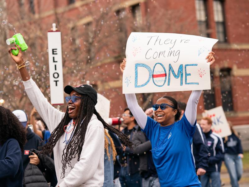 Students holding up a sign for Eliot House that reads "they're coming dome".
