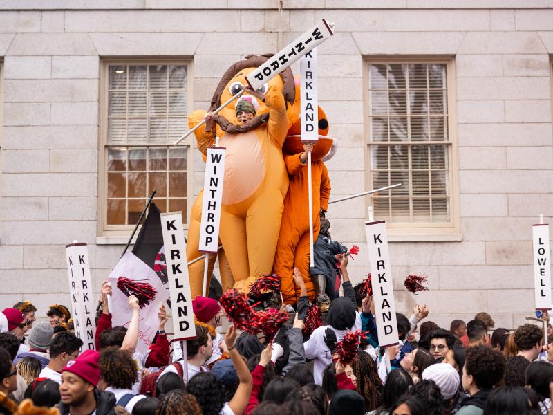 Two male students in inflatable lions costumes standing on top the John Harvard statue.