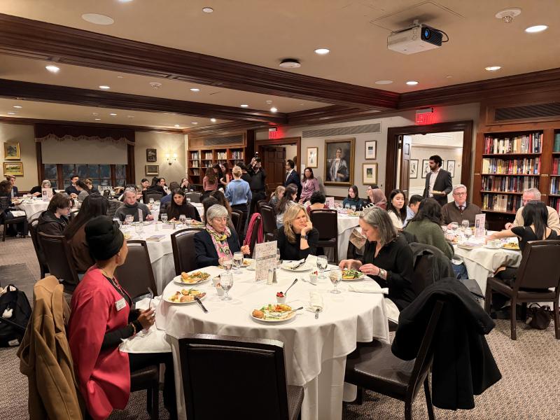 Guests seated at round tables enjoy dinner and conversation in a formal, book-lined event room.