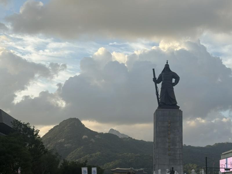 Picture of a plaza in the afternoon with a statue and people walking around