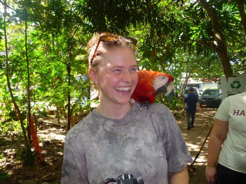 A student poses with a colorful red bird perched upon her left shoulder.