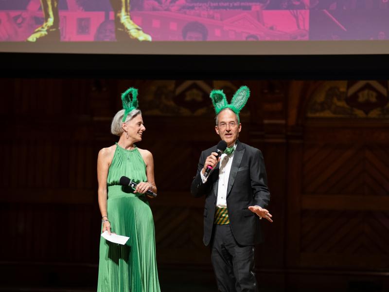 Leverett House Faculty Deans Eileen Reynolds & Dan Deschler onstage wearing green rabbit ears for Leverett.