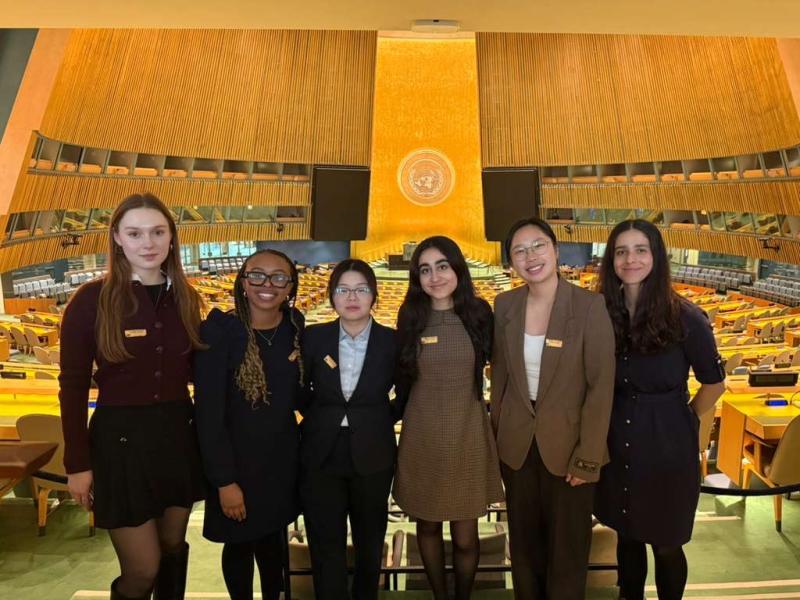 Students stand together smiling in the UN General Assembly hall.