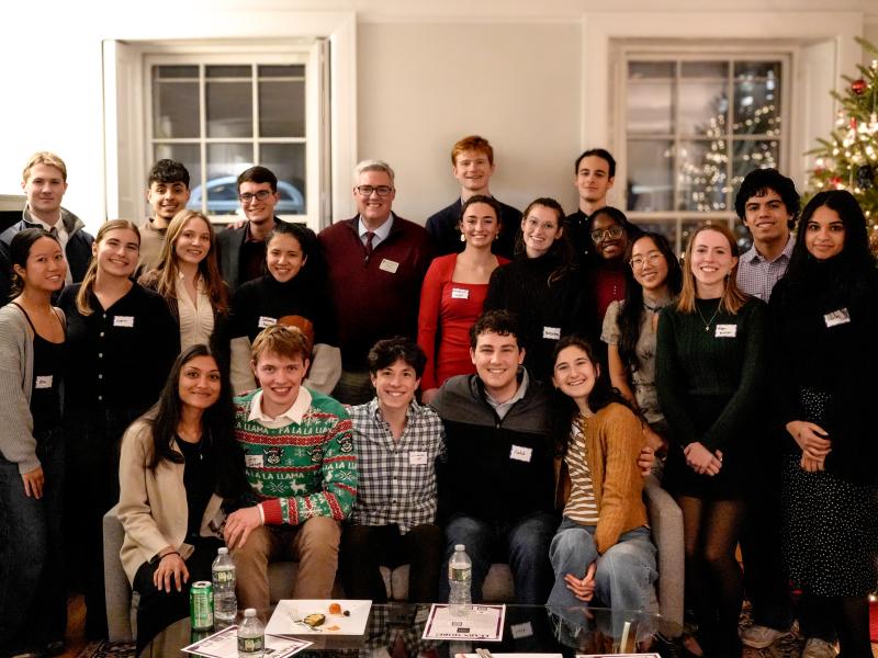 Large group of students and a faculty member pose together in a festive living room with a Christmas tree.