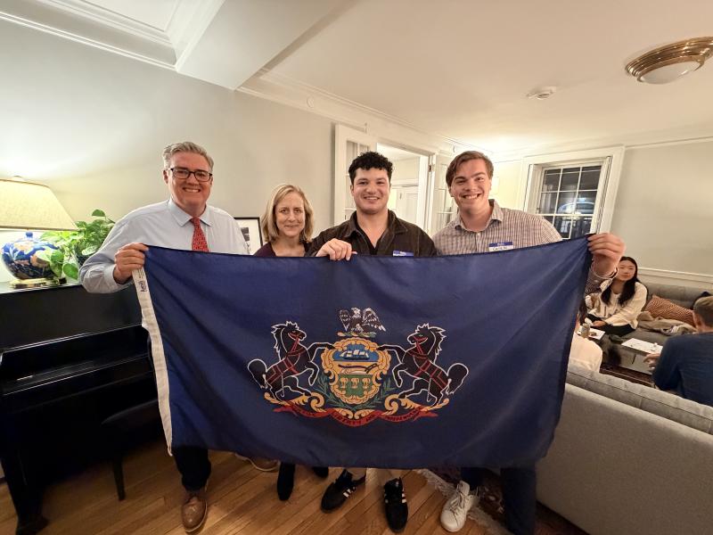 Four people stand in a living room holding a large Pennsylvania state flag.