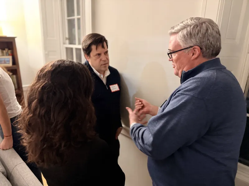 Two adults and a student stand near a wall, engaged in a close conversation.