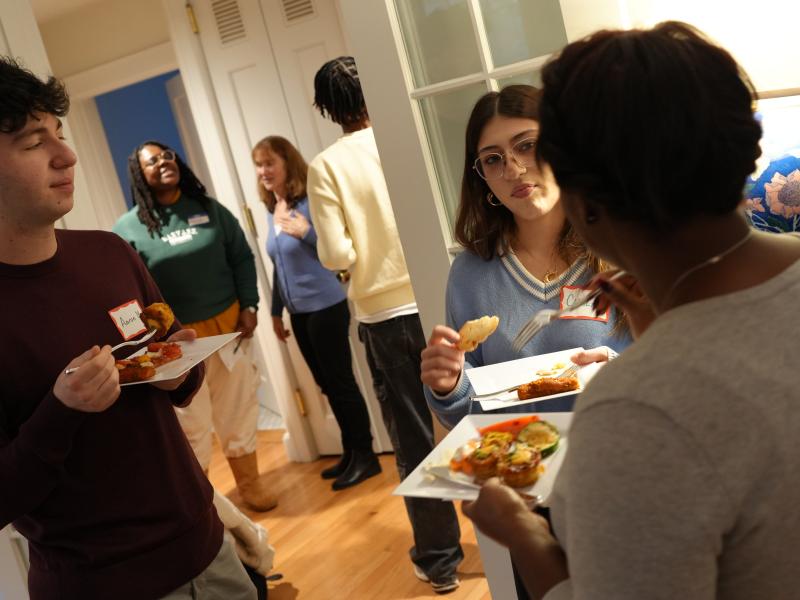 Students chat and eat from small plates during a casual indoor reception.