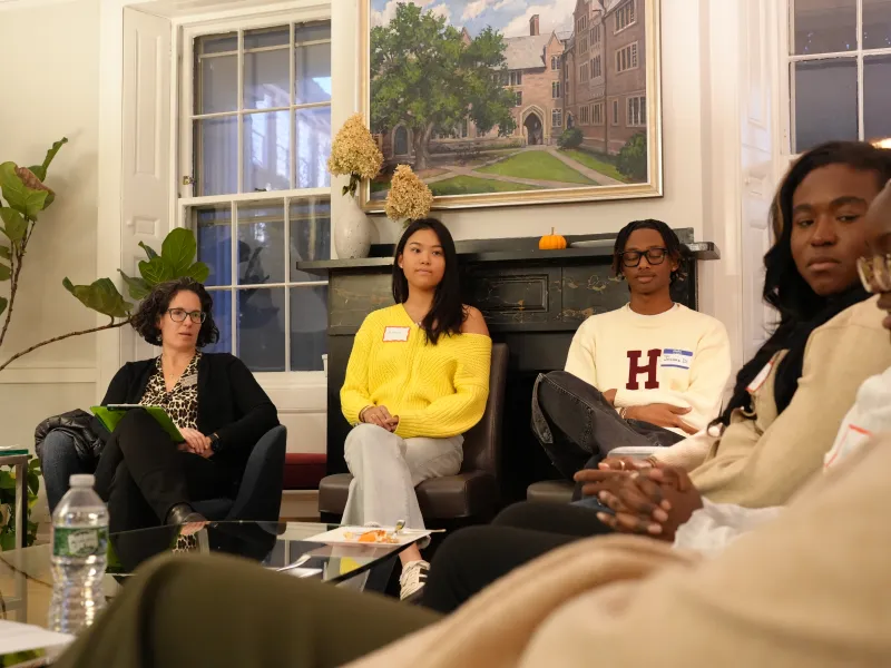 Students and a staff member sit in a circle in a cozy living room, listening during a discussion.