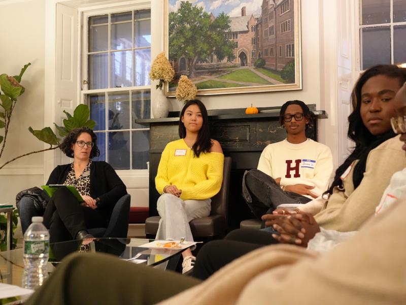 Students and a staff member sit in a circle in a cozy living room, listening during a discussion.