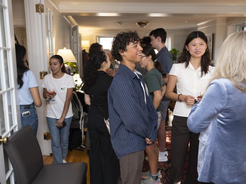 A group of people talk and smile during an indoor social gathering in a room with hardwood floors and white French doors.