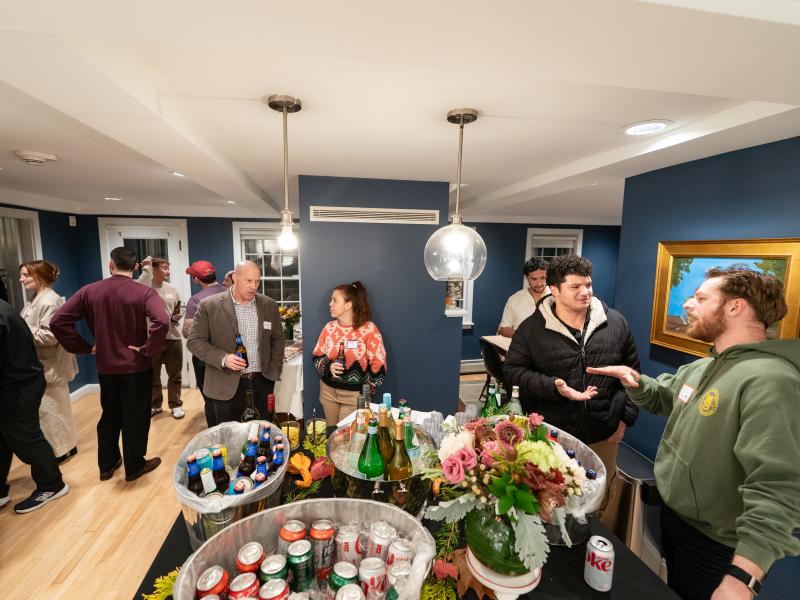 Guests mingle in a room with blue walls, featuring a table in the foreground stocked with ice-filled beverage buckets and flowers.