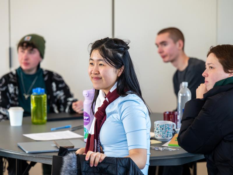 Four students sitting at a round table listening and all looking to the left.