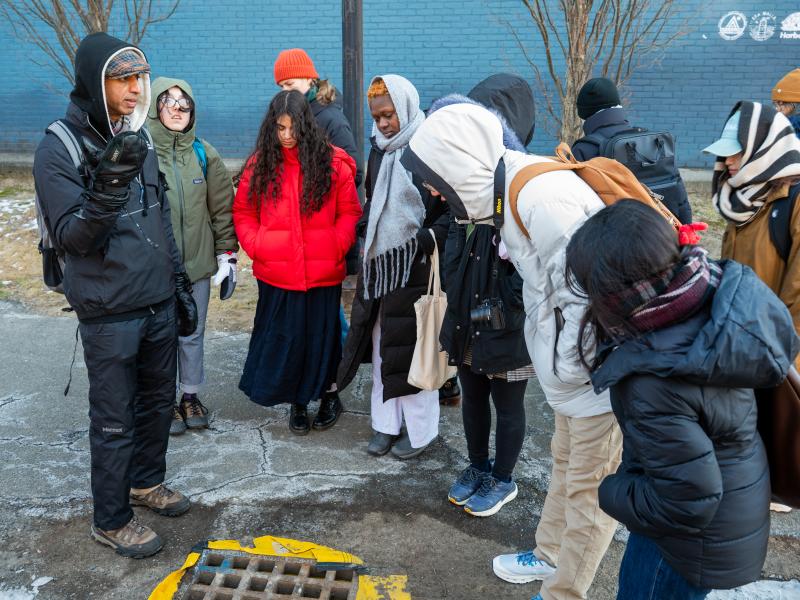 Students crowded around a storm drain and looking down at it.