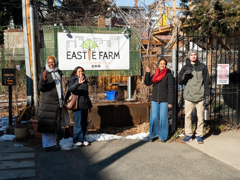 Four students standing next to the Eastie Farm sign and smiling.