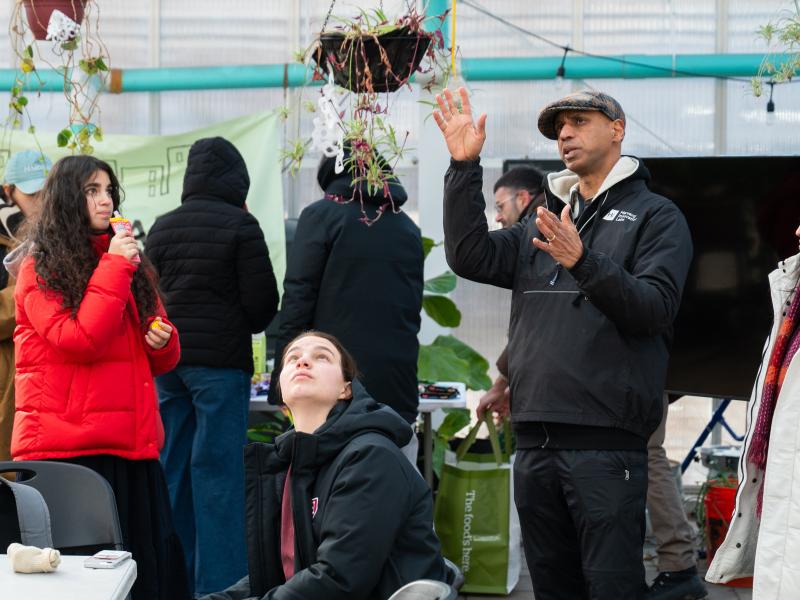 Kannan pointing to a hanging plant inside Eastie Farm, with students looking up at it.