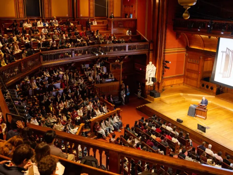 A lecture held in Sanders Theater with the word VISITAS projected onto a screen.