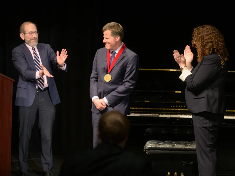 President Alan Garber ‘76 (left), 2026 Harvard Arts Medalist Bill Rauch ‘84 (center), and Office for the Arts Director Fiona Coffey (right). 