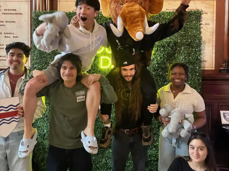 A group of first-years taking pictures in front of a housing day backdrop in Memorial Hall