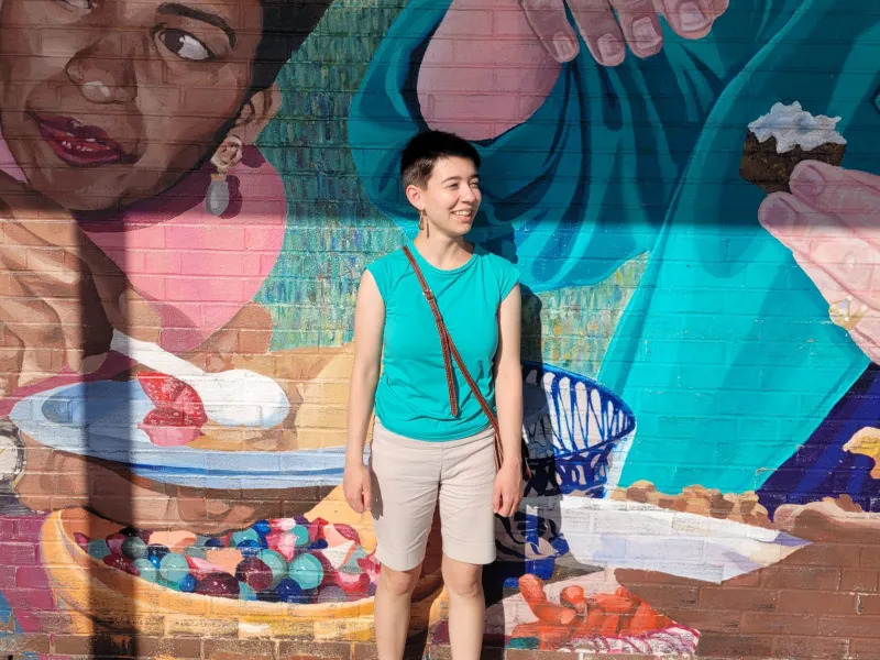 A student stands in front of a colorful mural