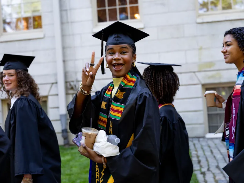 A female student in regalia gives a peace sign to the camera.