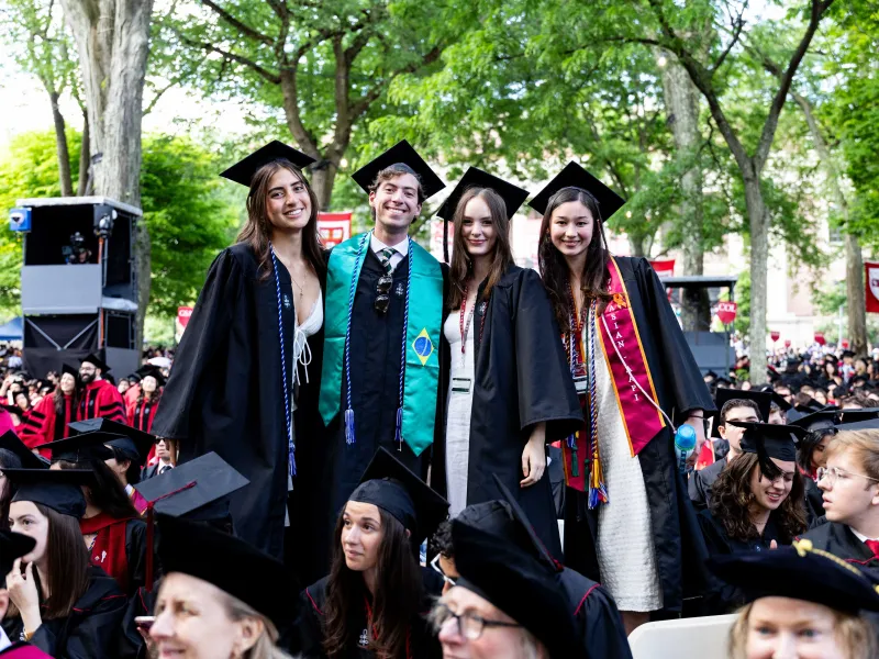 Four graduates standing up from their seats to smile together for a photo.