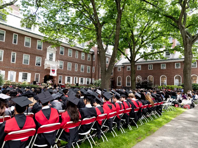 A wide shot of the graduates seated in rows at Kirkland House on one side, and guests on the other side.