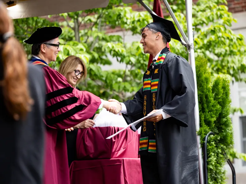 A male student shakes hands with faculty while onstage accepting his degree.