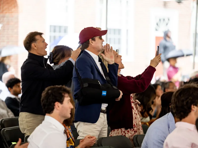 Side profile of four parents yelling for their graduating child and recording the moment on their cellphones.