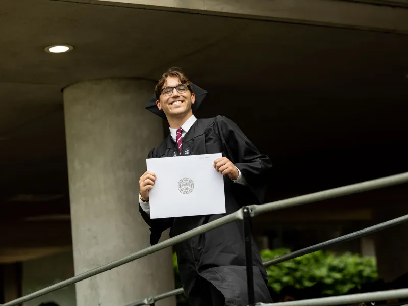A male student holding up his degree and smiling.