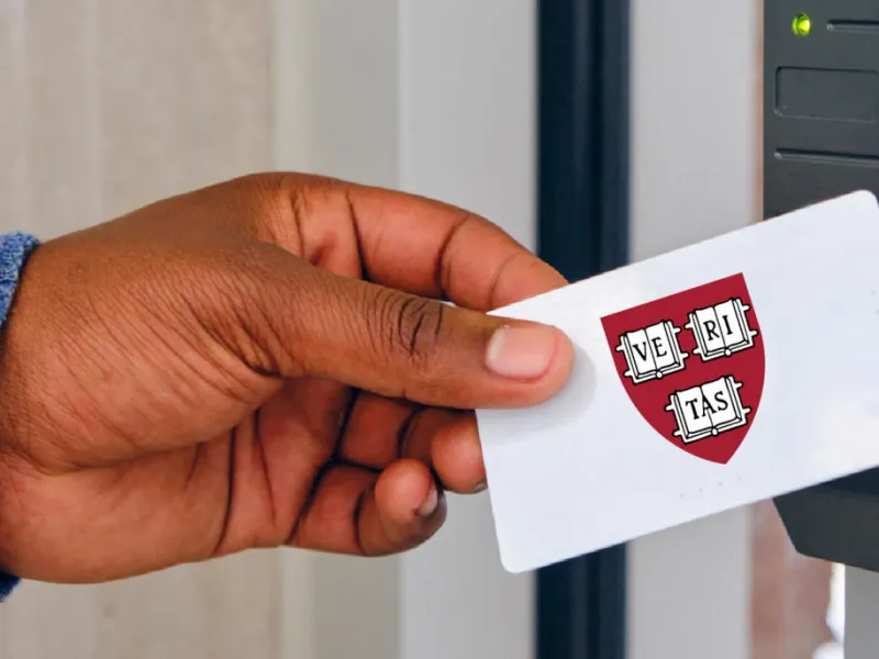 A hand holding a card featuring a Harvard ID with the Harvard crest
