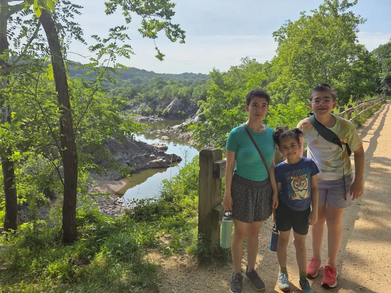 Three siblings stand in front of an overlook that looks down on a river.