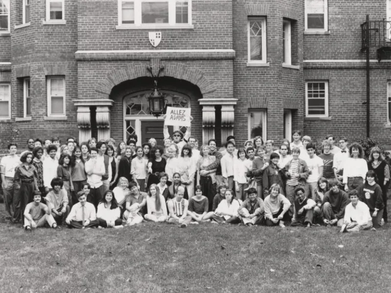 A black and white image of students gathered for a photo outside of Adams House.