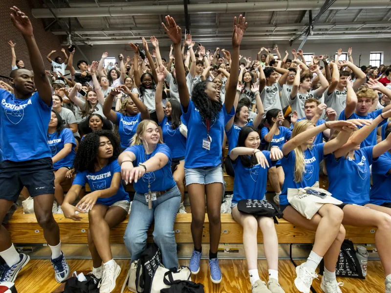 A large group of students in blue shirts lifting up their hands and cheering together.