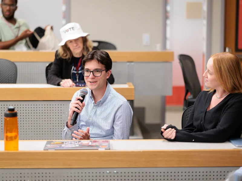 Harvard College student Jordan Schwartz '27 speaking into a microphone while sitting at a desk with another student.