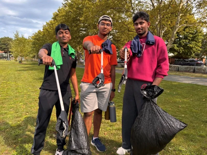 Three male students in the park holding up trash bags while cleaning up Harambe Park.