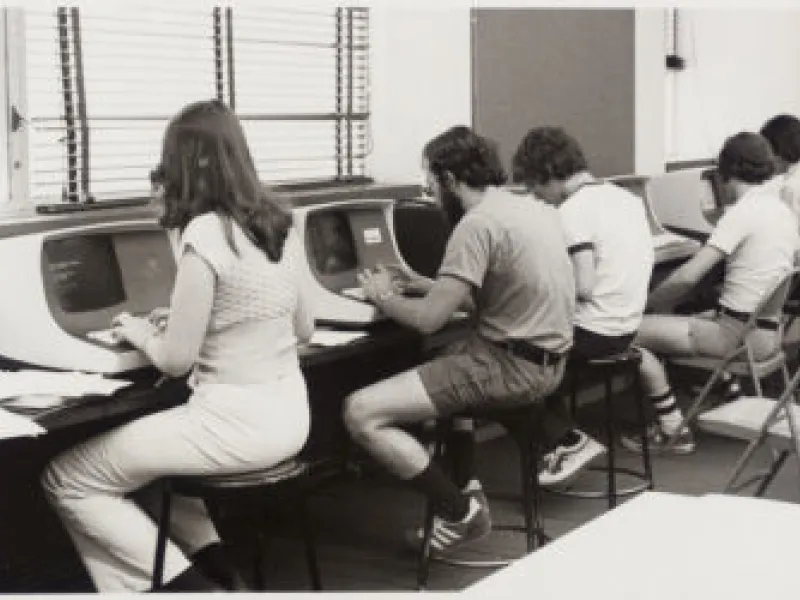 A black and white image of students working on desktop computers in 1977.