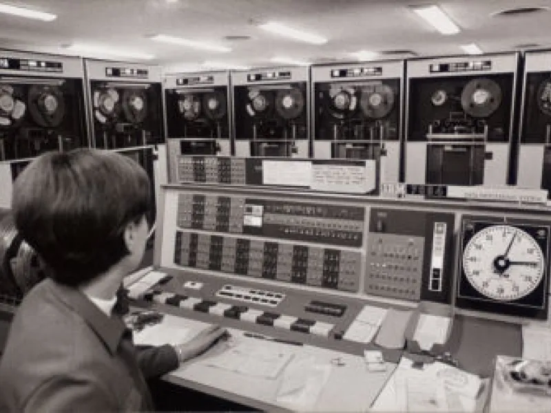 A black and white image of a man sitting in a computation lab in the 1960s.
