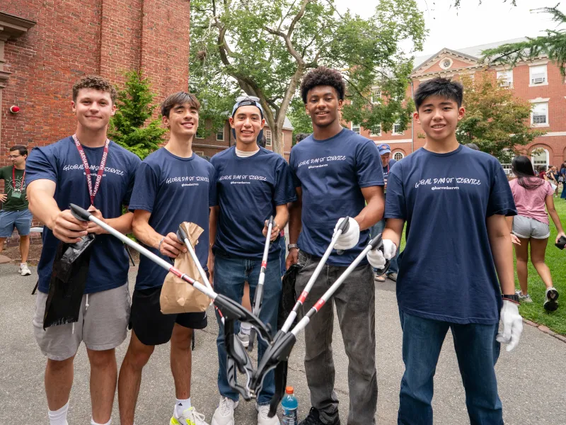 A group of 5 male students holding items to pick up trash.